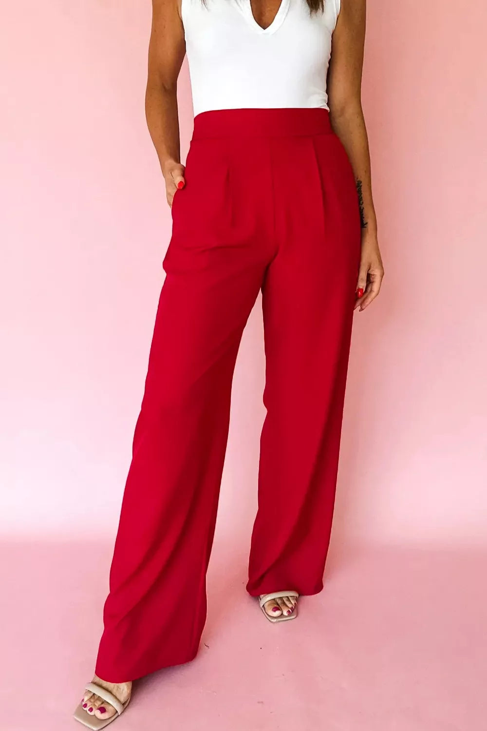 Person wearing red pants and a white top on a pink background