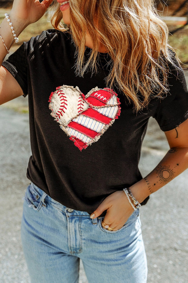 Person wearing a black t-shirt with a heart design featuring a baseball and American flag, standing outdoors.