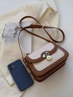 Small brown and beige handbag with a decorative clasp next to a blue phone on a light fabric background.