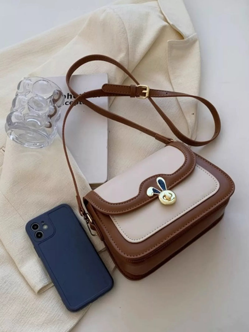 Small brown and beige handbag with a decorative clasp next to a blue phone on a light fabric background.