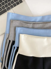 Stack of folded clothes including a blue shirt, gray pants, and black shorts on a light surface.
