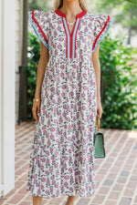 Woman wearing a floral dress with red and blue accents, standing outdoors on a brick path.