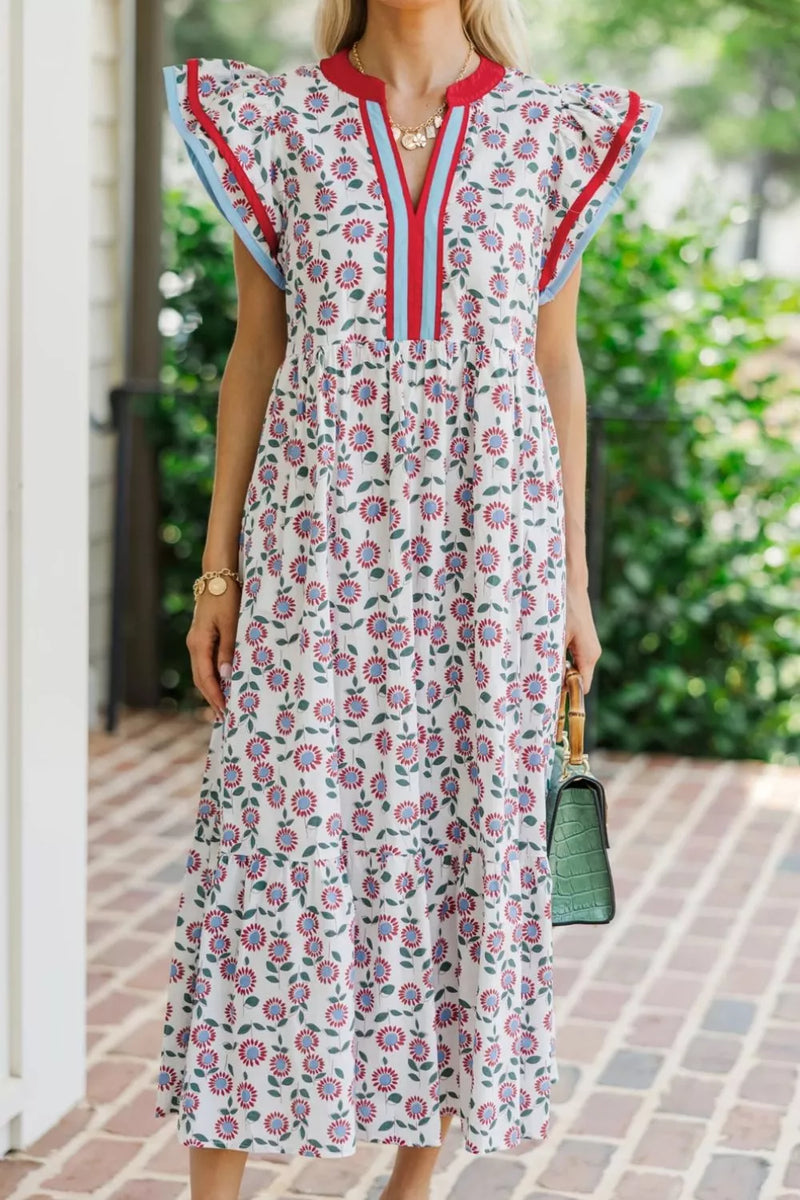 Woman wearing a floral dress with red and blue accents, standing outdoors on a brick path.