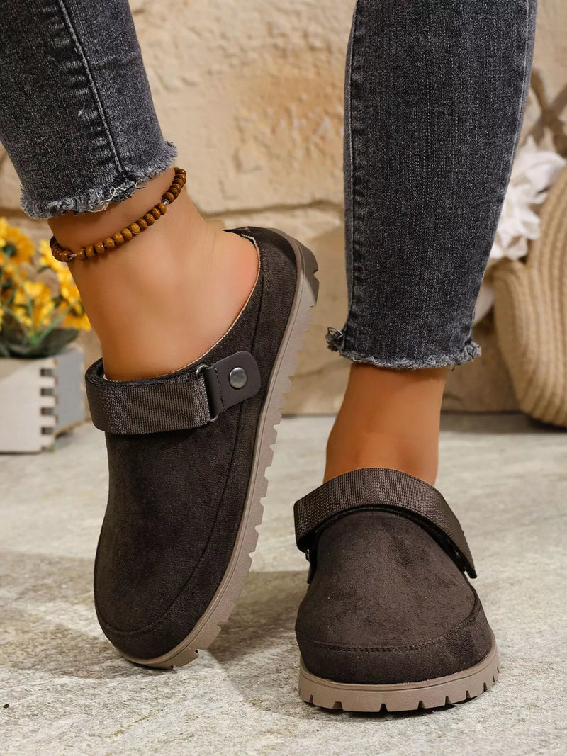 Brown clogs worn with jeans on a stone floor.