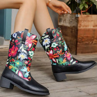 Black rain boots with colorful floral patterns worn by a person sitting on a wooden floor.