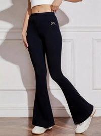 Person wearing black flared pants with a white bow detail in a minimalistic setting.