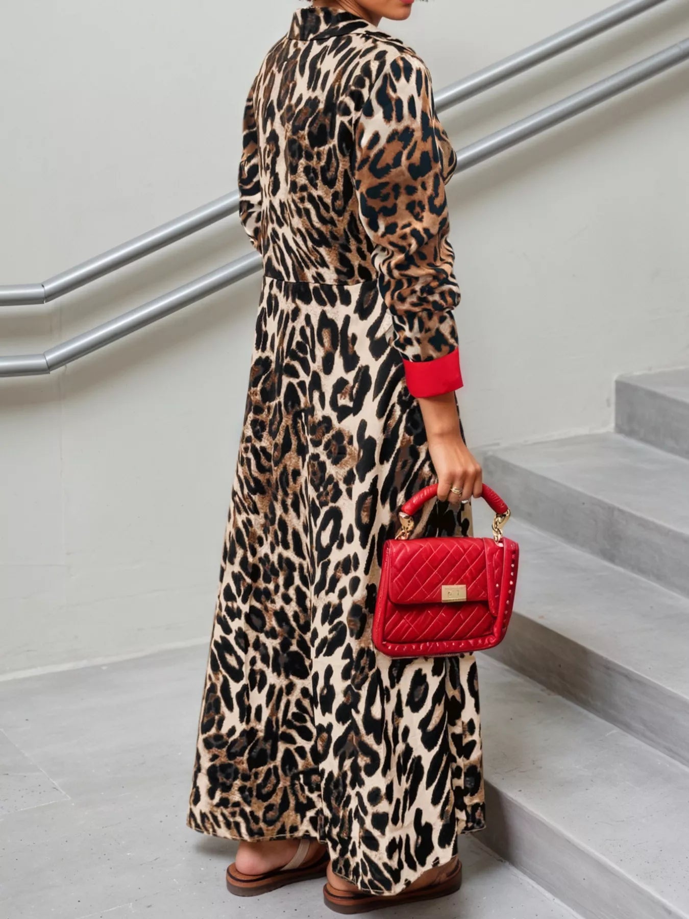 Person wearing a leopard print dress holding a red handbag on a staircase.
