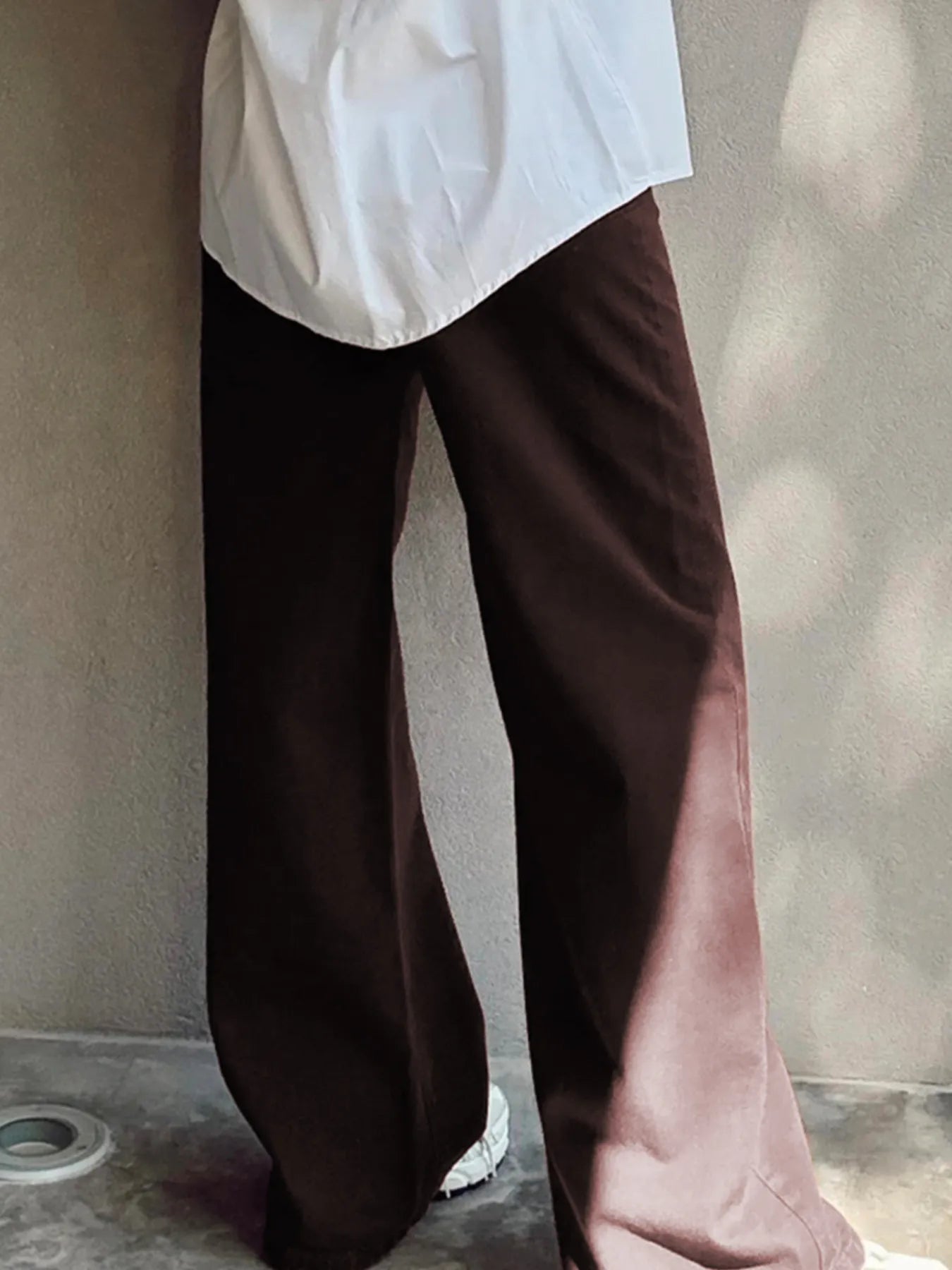 Brown wide-leg pants worn with a white shirt against a neutral background