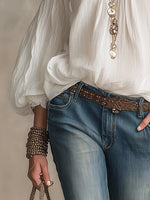Person wearing a white blouse, blue jeans, and a decorative belt with a neutral background