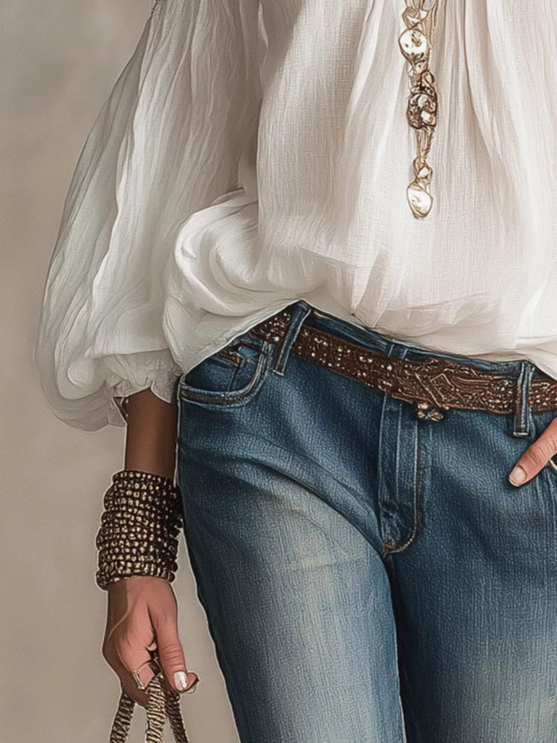 Person wearing a white blouse, blue jeans, and a decorative belt with a neutral background