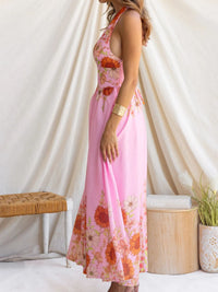 Woman wearing a pink floral dress standing against a white curtain.
