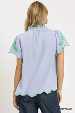 Light blue blouse with green embroidery on a plain background