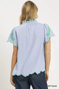 Light blue blouse with green embroidery on a plain background