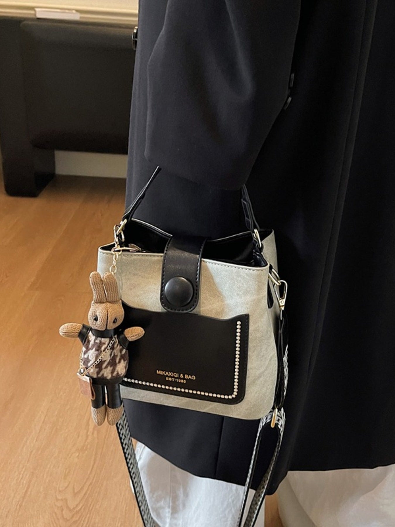 Person holding a black and white handbag with a small rabbit-shaped bag charm.