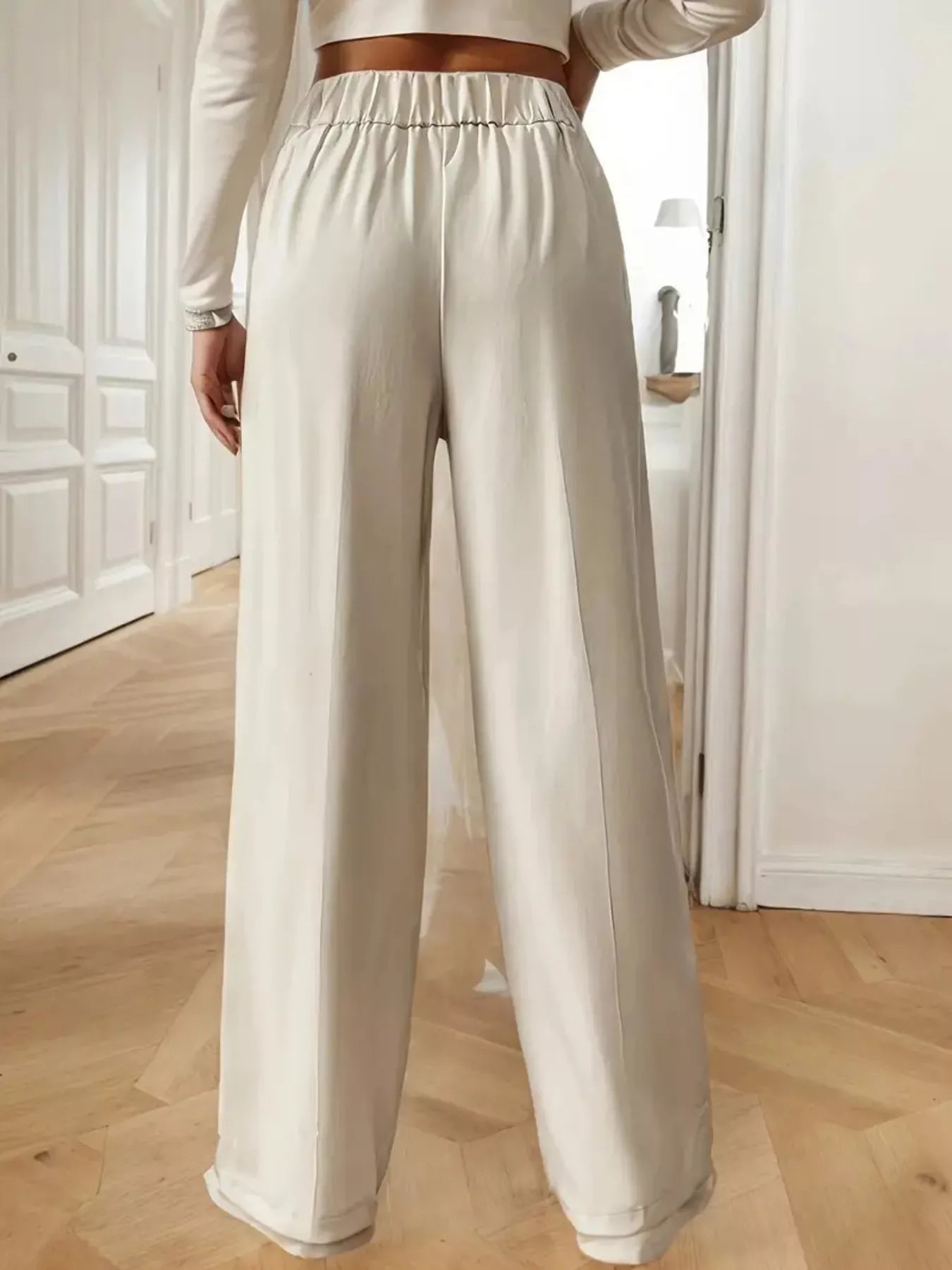 Person wearing light-colored pants in a room with wooden flooring and white walls.