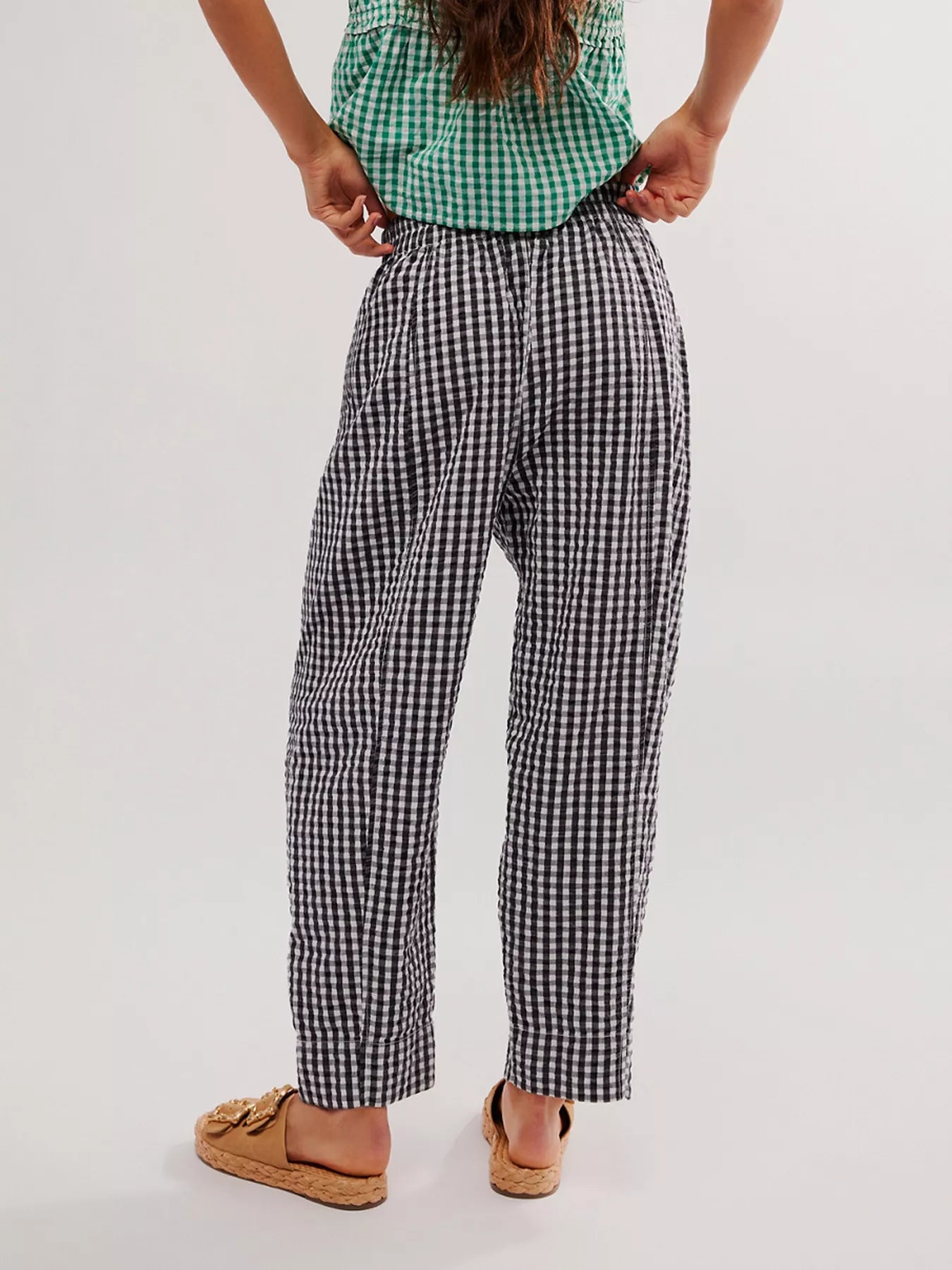 Person wearing a green checkered shirt and black and white checkered pants on a plain background