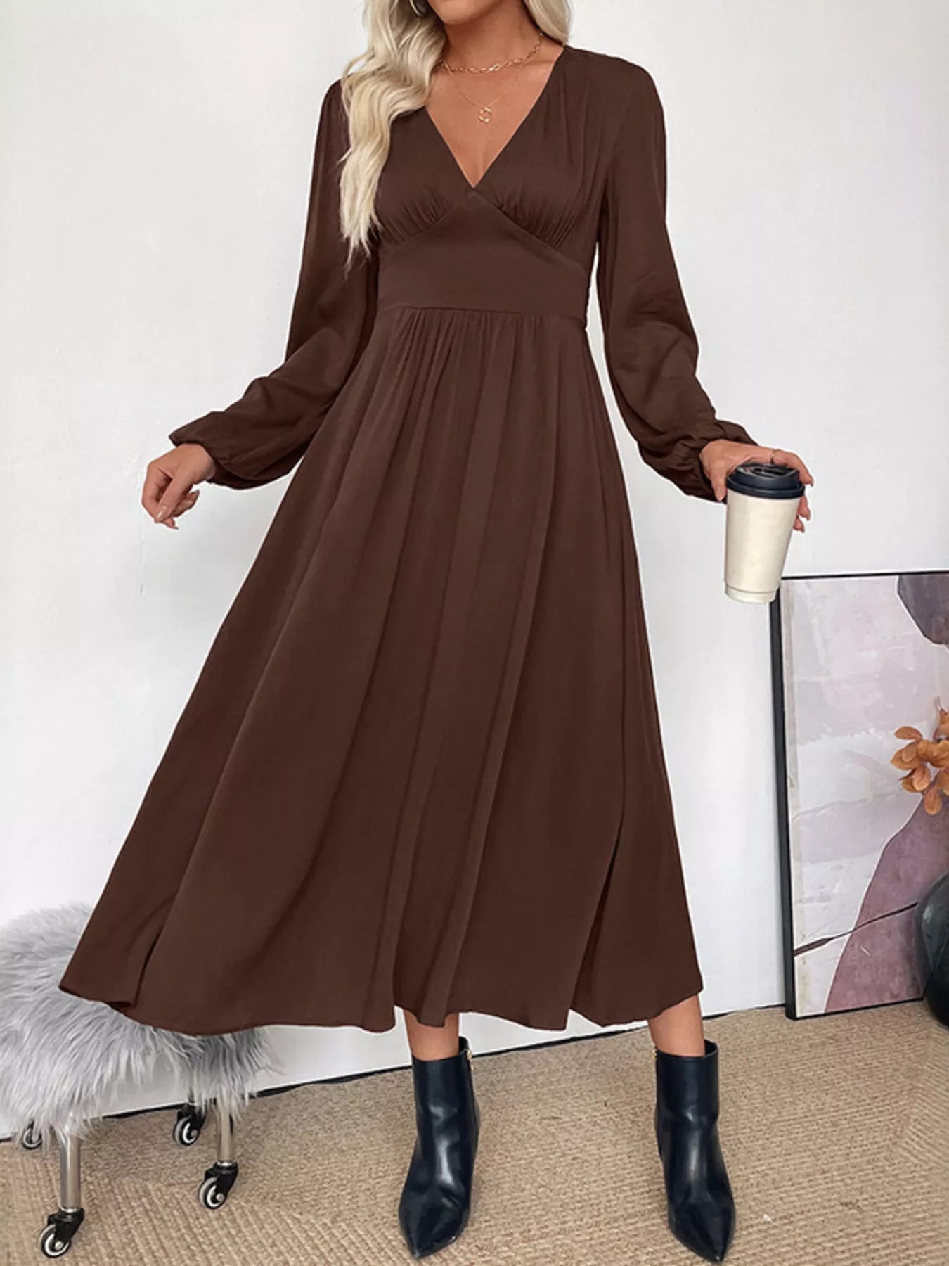 Woman wearing a brown dress holding a coffee cup against a white wall.