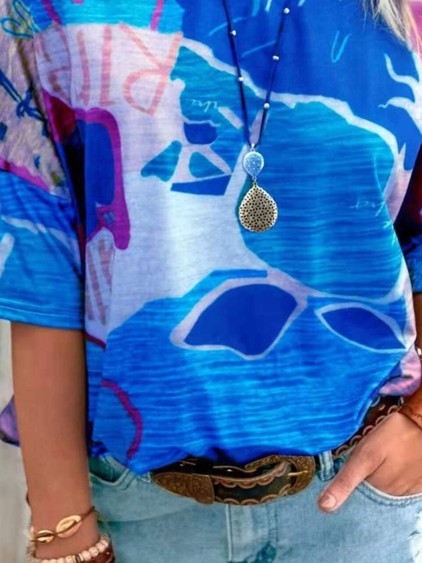 Person wearing a colorful shirt with abstract designs and a necklace.