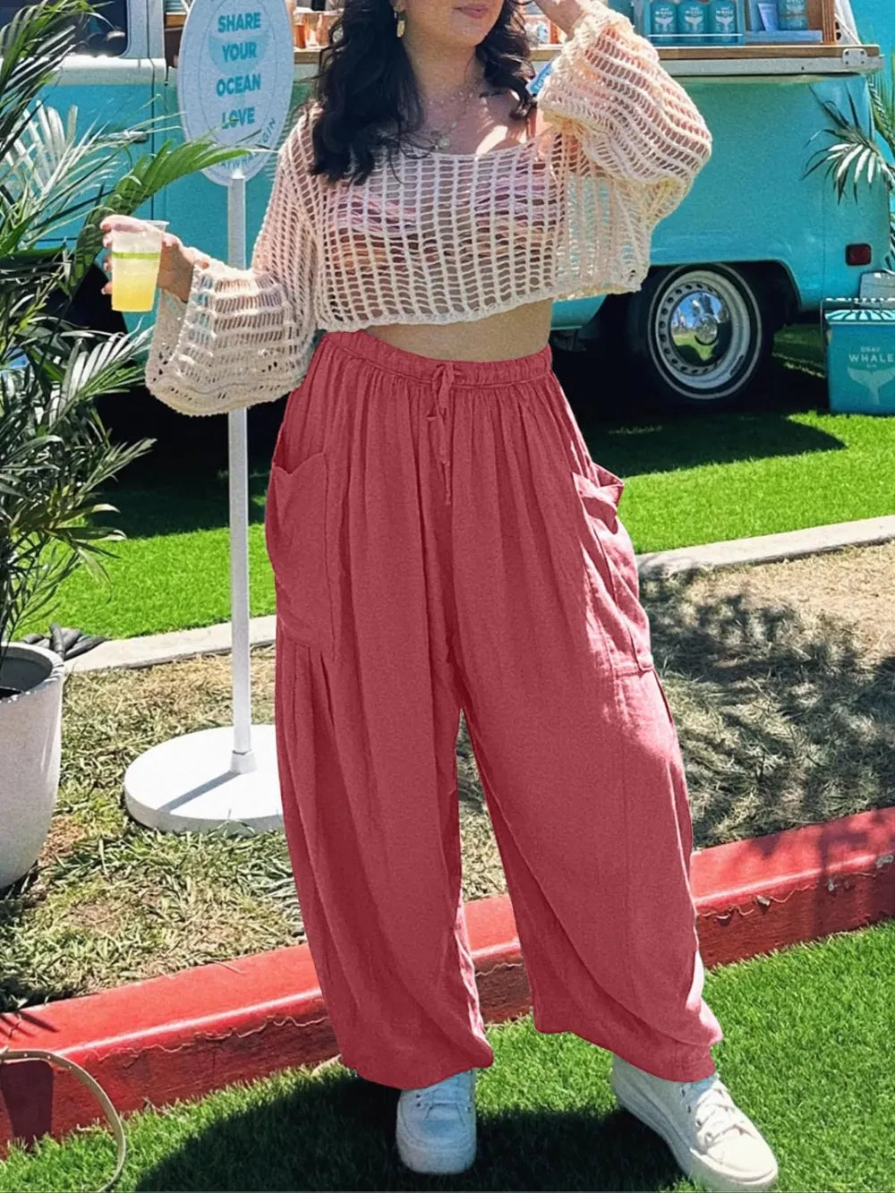 Woman in a baggy pants outside on a lawn with drink in her hand