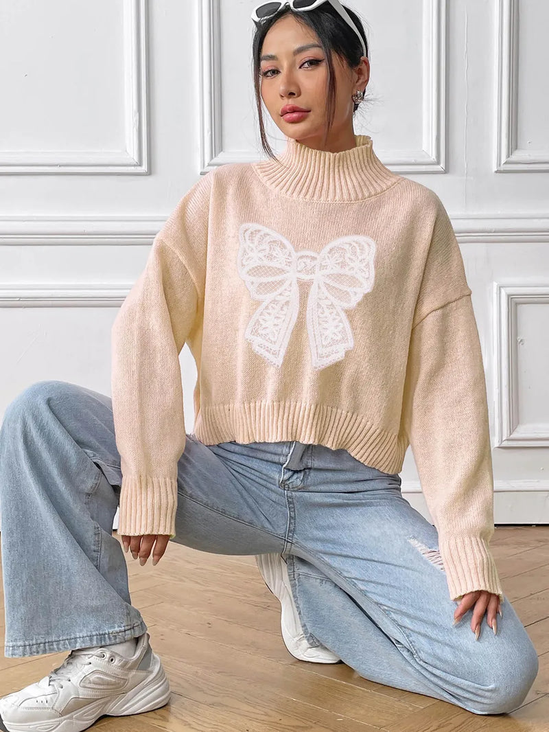 Person wearing a beige sweater with a butterfly design and light blue jeans, sitting on the floor.