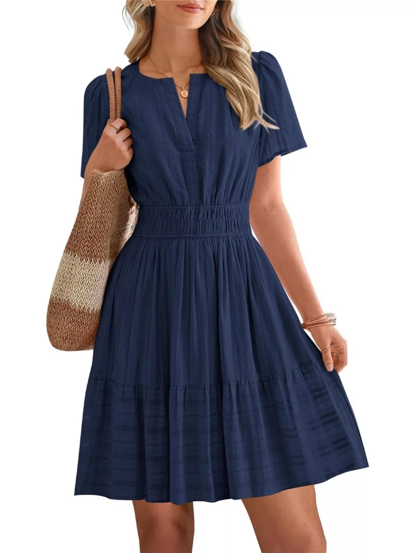Woman wearing a navy blue dress holding a brown bag on a white background