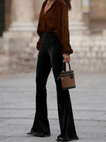 Person wearing a brown blouse and black pants holding a brown handbag on a street.