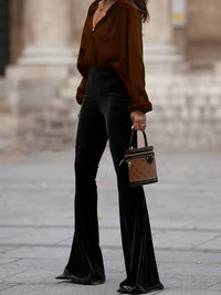 Person wearing a brown blouse and black pants holding a brown handbag on a street.