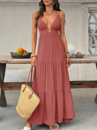 Woman in a long pink dress holding a straw bag in an outdoor setting.