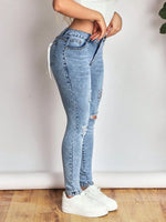 Person wearing light blue jeans and white sneakers on a wooden floor with a white wall background