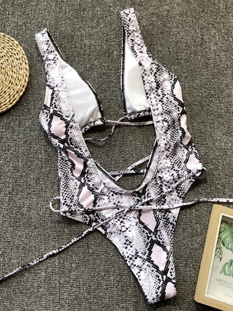 Snake print bikini set on a textured surface with a woven mat and framed picture in the background.