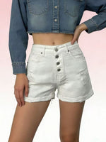 Person wearing white denim shorts with button details on a pink background