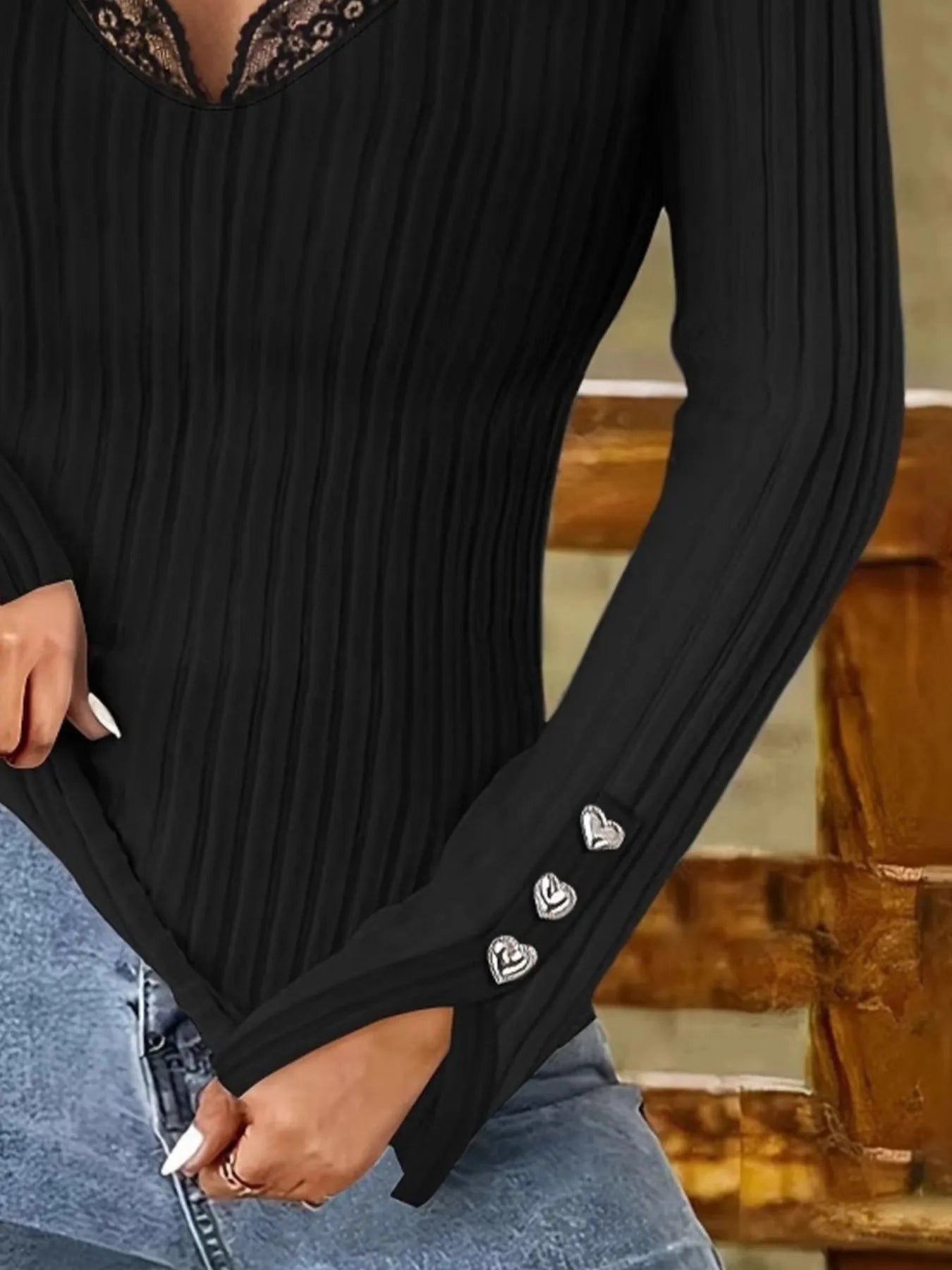 Black ribbed long-sleeve top with decorative heart details on a blurred background