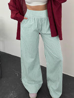 Person wearing green checkered pants with a red jacket on a plain background