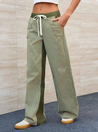 Person wearing green corduroy pants with a beige wall background