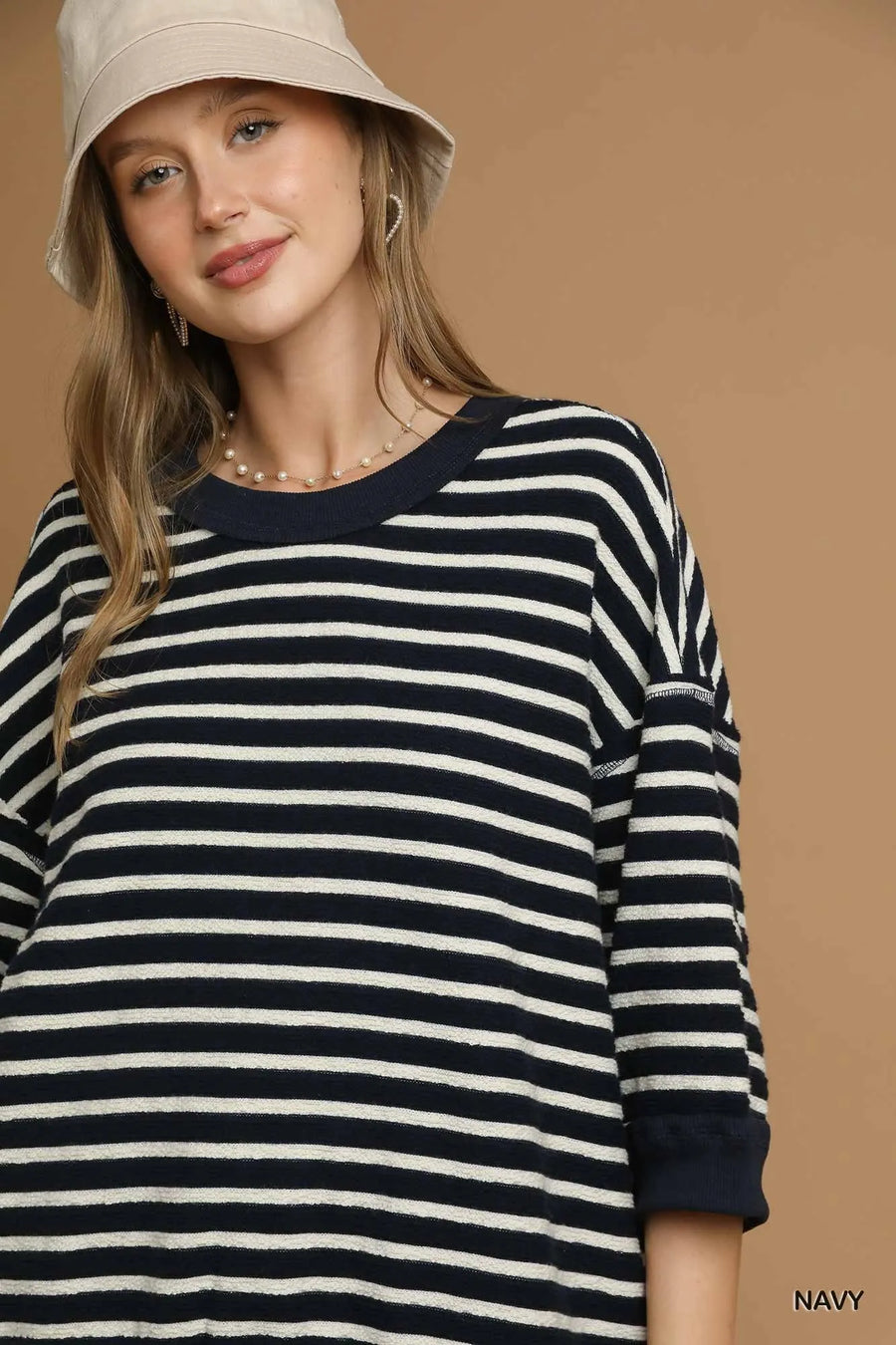 Woman wearing a navy and white striped sweater with a beige hat on a brown background
