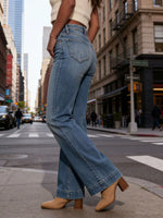 Person wearing blue jeans and beige shoes on a city street.