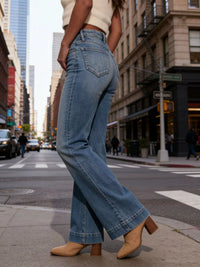 Person wearing blue jeans and beige shoes on a city street.