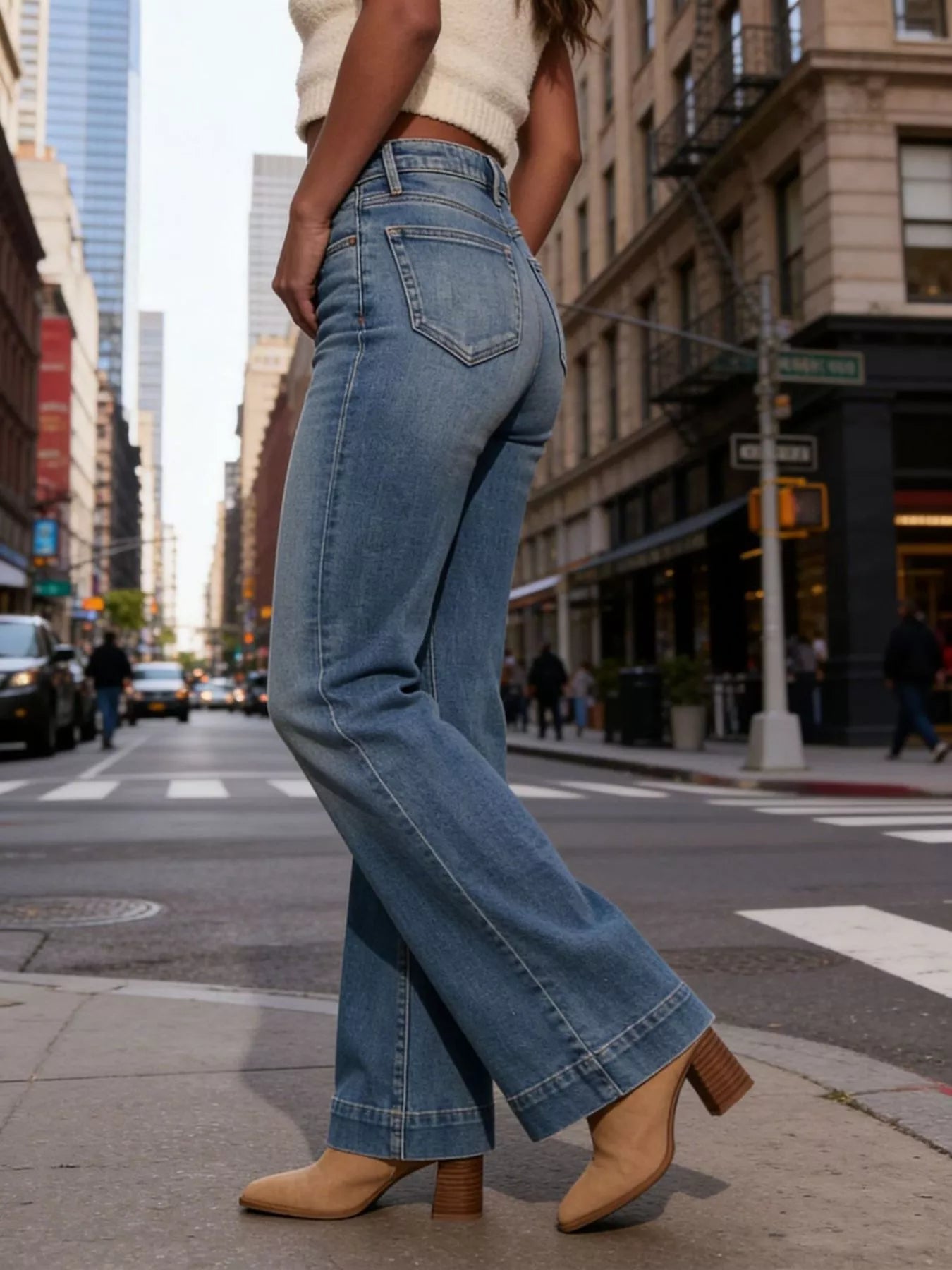 Person wearing blue jeans and beige shoes on a city street.