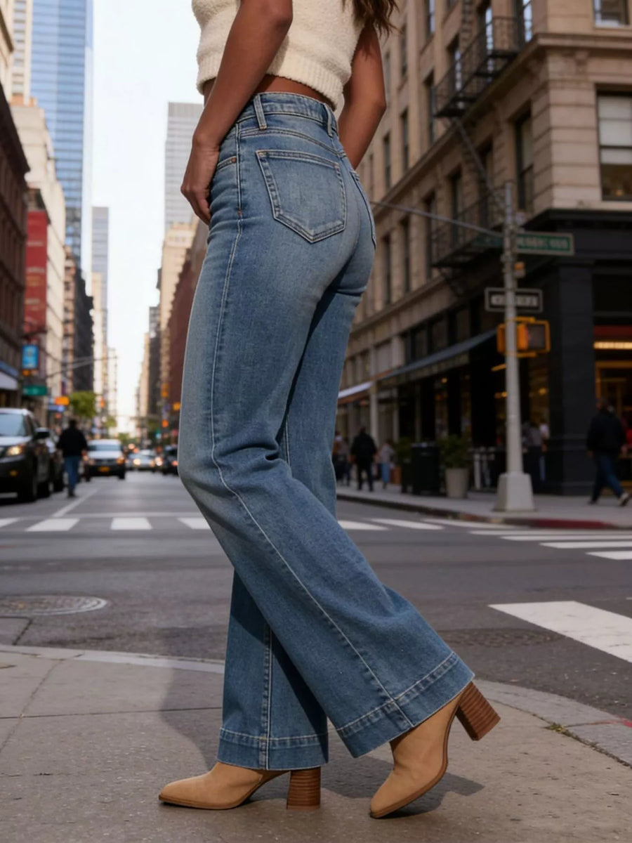 Person wearing blue jeans and beige shoes on a city street.