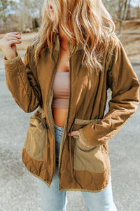 Person wearing a brown jacket outdoors with a blurred background