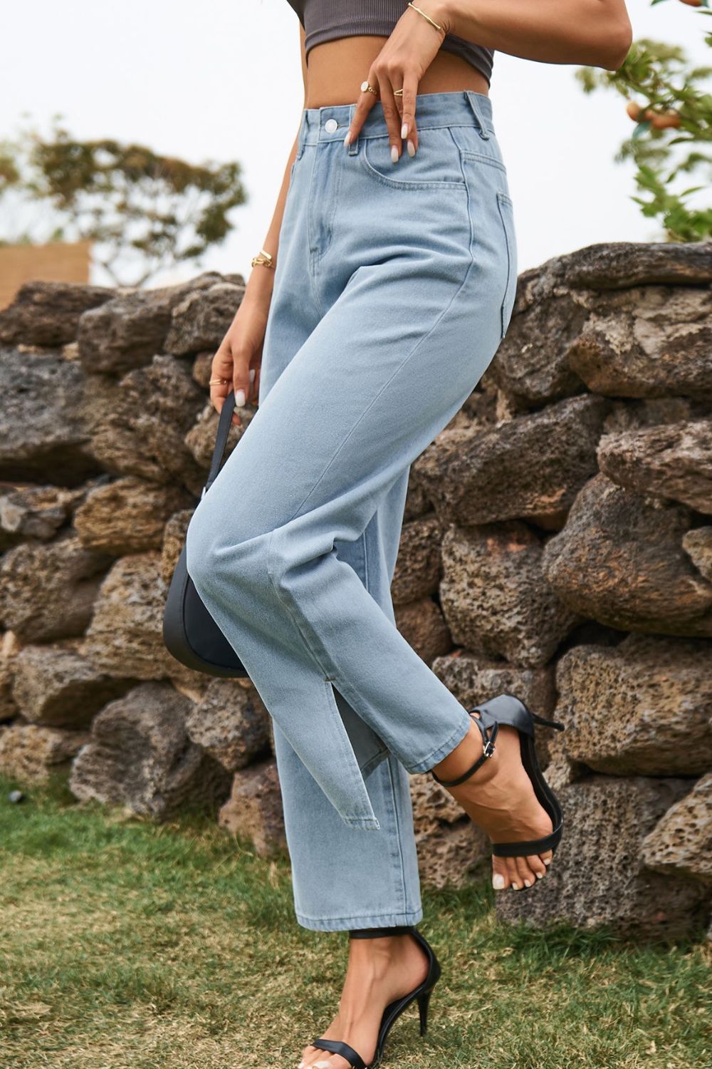 Person wearing light blue jeans standing against a stone wall.