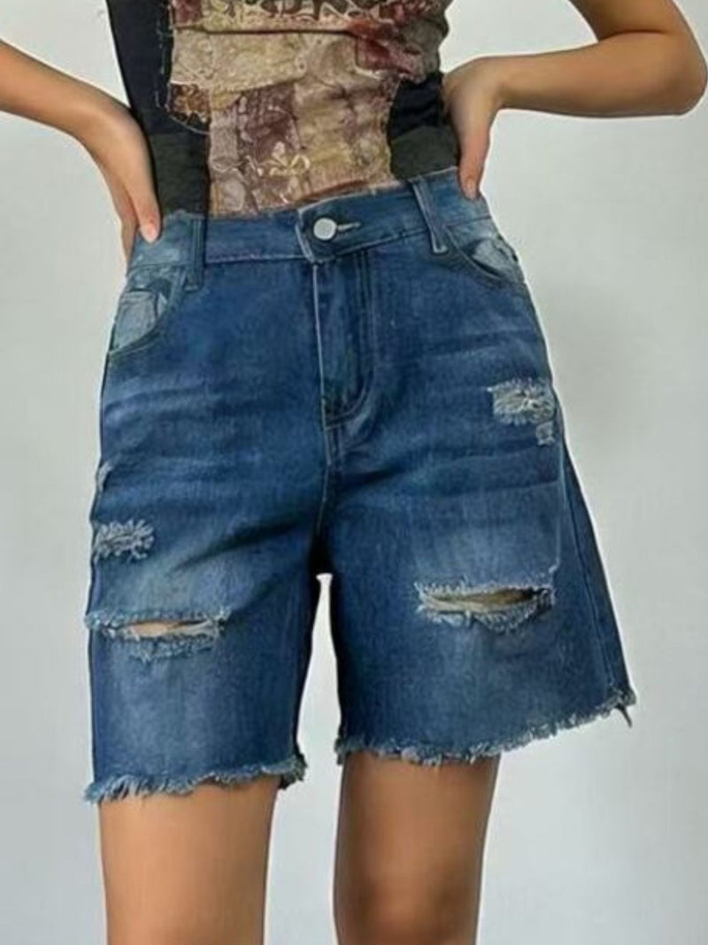 Person wearing blue denim shorts with distressed details on a plain background