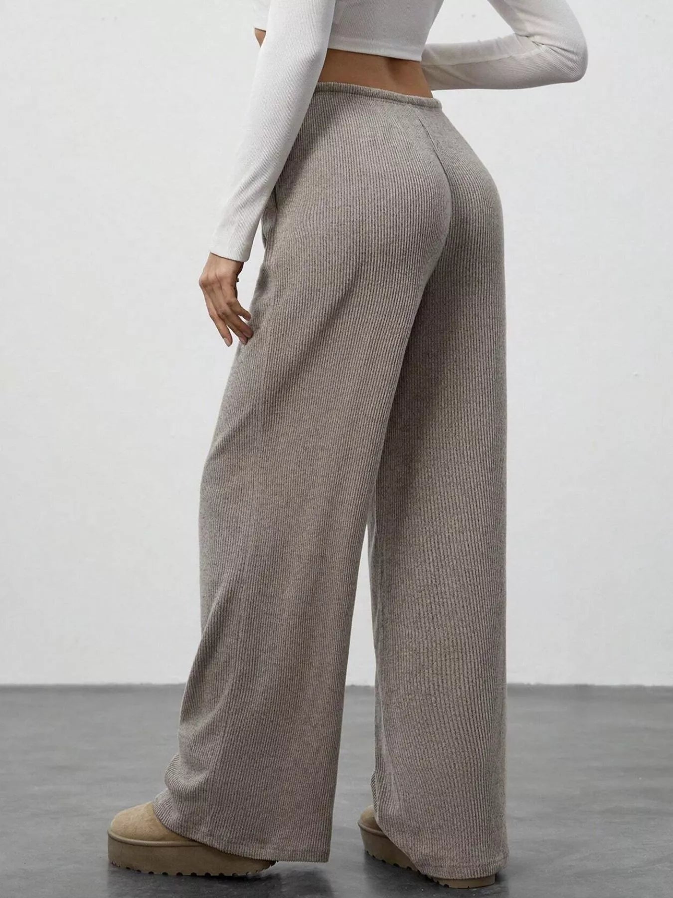 Person wearing beige ribbed wide-leg pants and a white long-sleeve top against a plain background