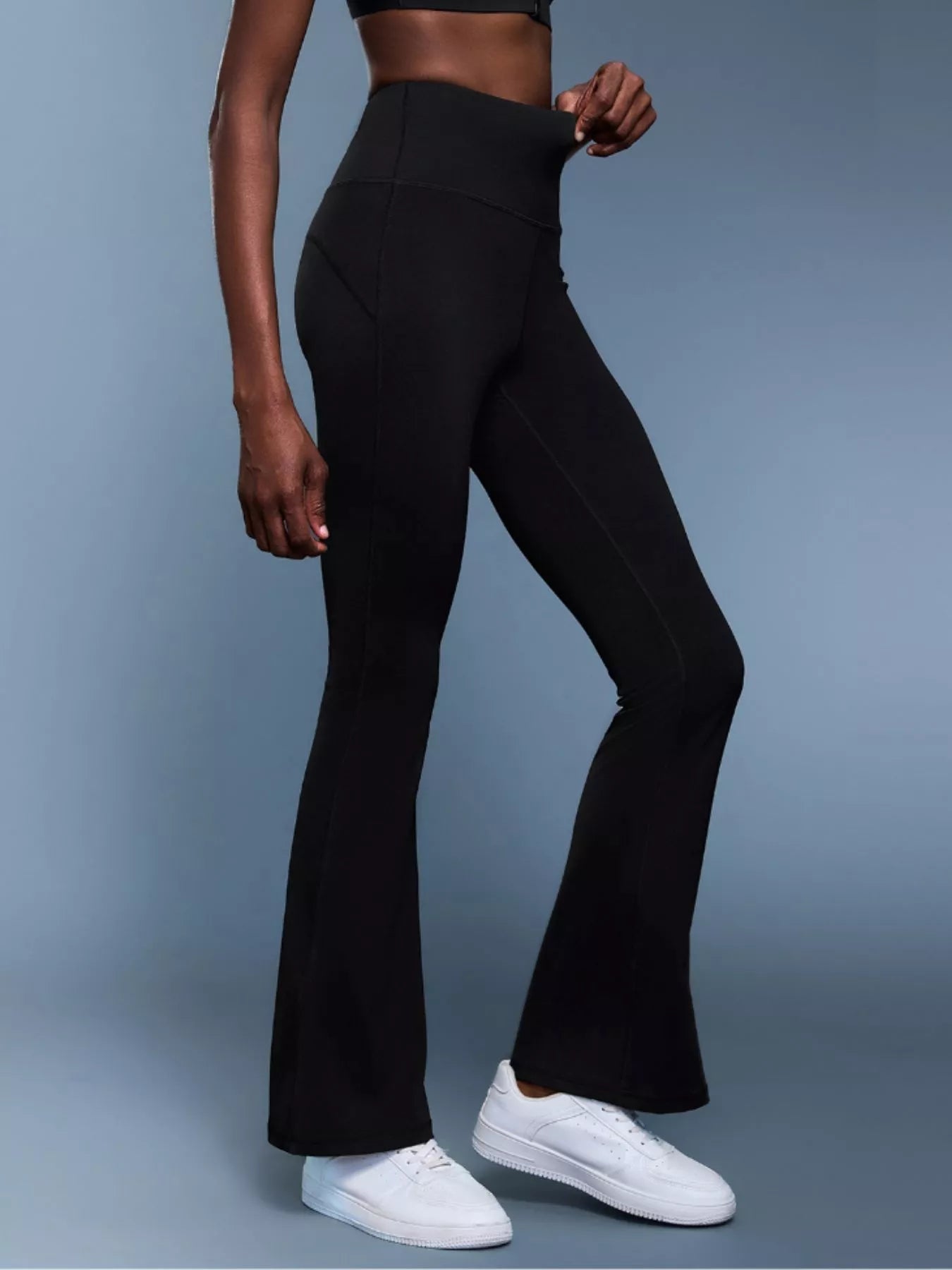 Person wearing black flared pants and white sneakers on a gray background