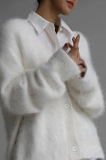 White fluffy cardigan worn over a white shirt on a gray background