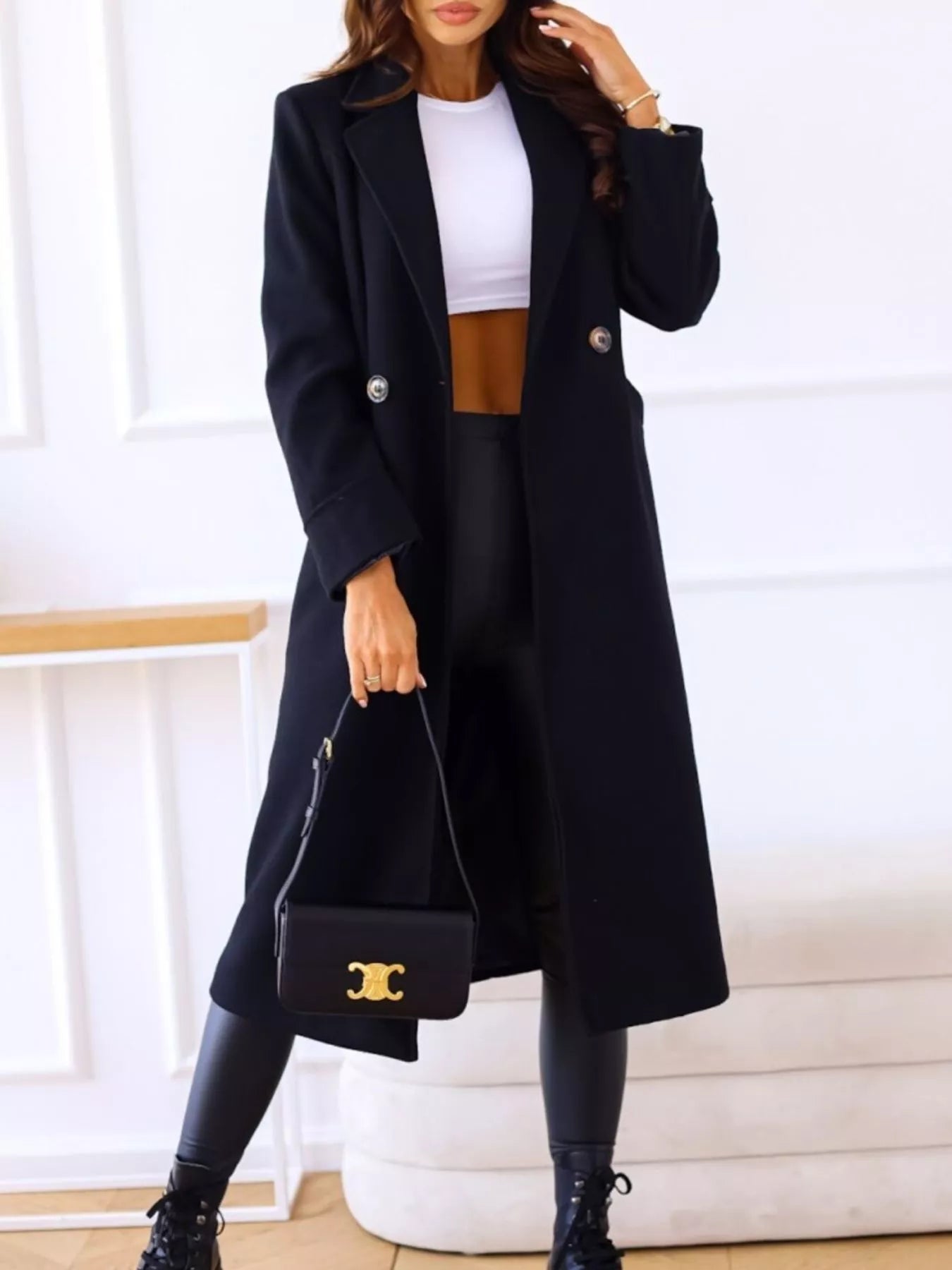 Person wearing a black coat, white top, brown skirt, and holding a black handbag with a gold logo.