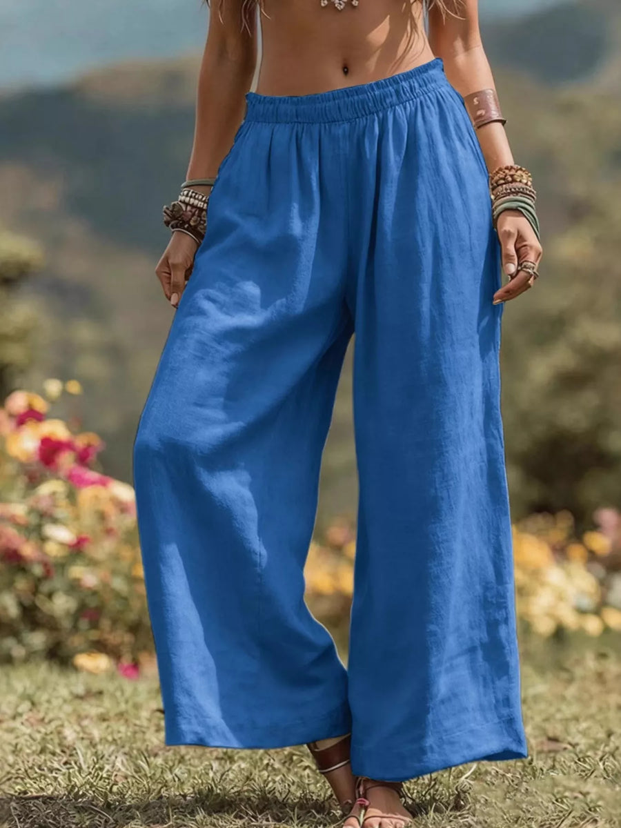Person wearing blue wide-leg pants standing in a natural setting with flowers and mountains.