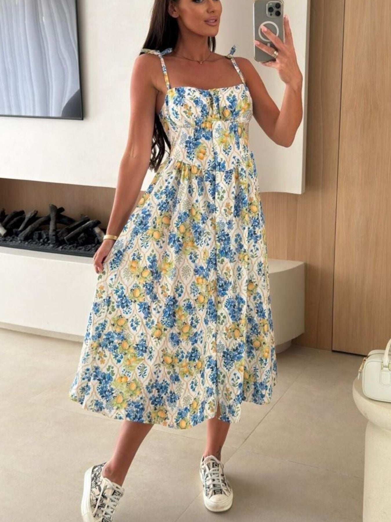 Woman taking a mirror selfie wearing a floral dress in a room.