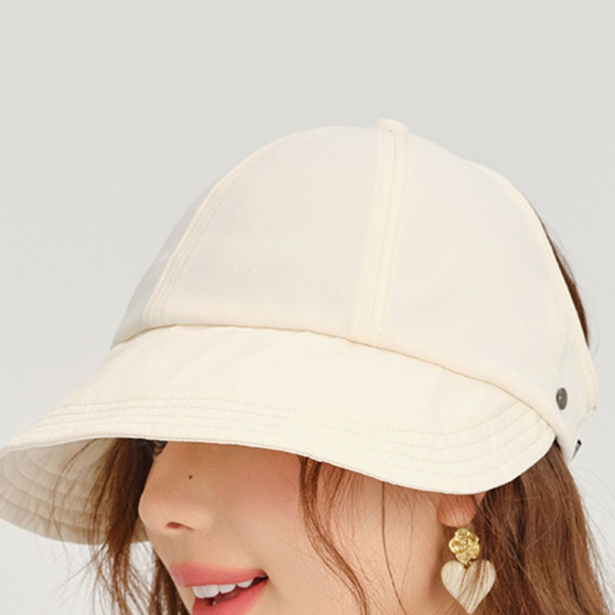 Close-up of a person wearing a beige bucket hat with a plain background