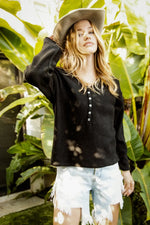 Woman wearing a black shirt and light denim shorts standing in front of large green leaves.